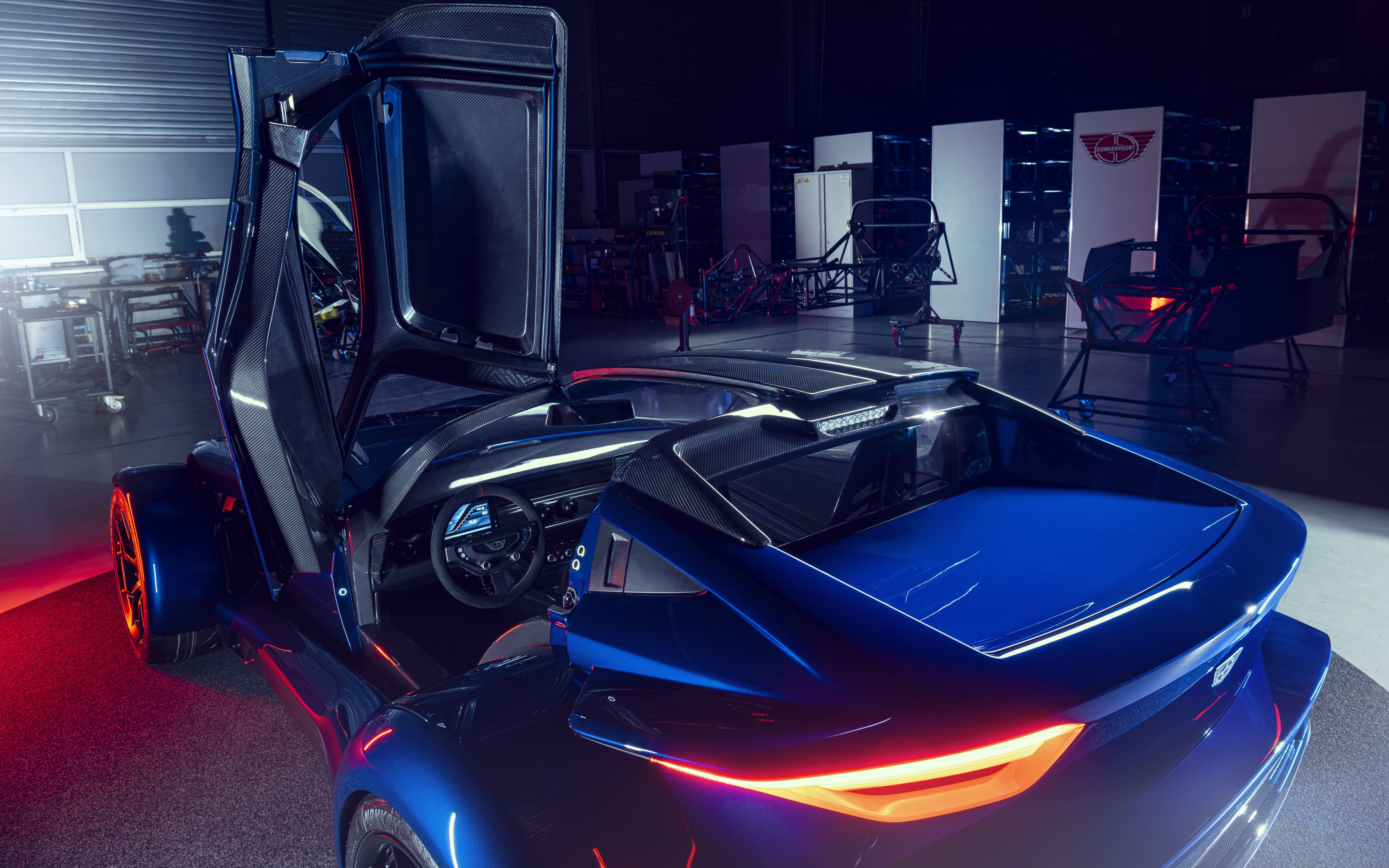 Un’elegante auto sportiva color argento metallizzato, che riflette la luce soffusa di un set fotografico su uno sfondo scuro.